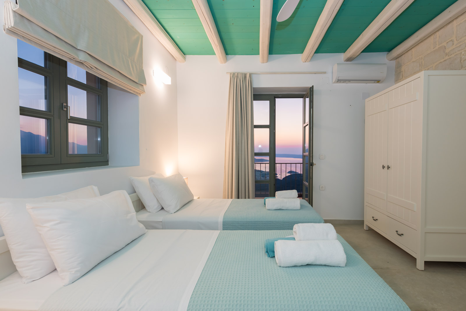 Twin bedroom with teal beamed ceiling, stone wall and balcony