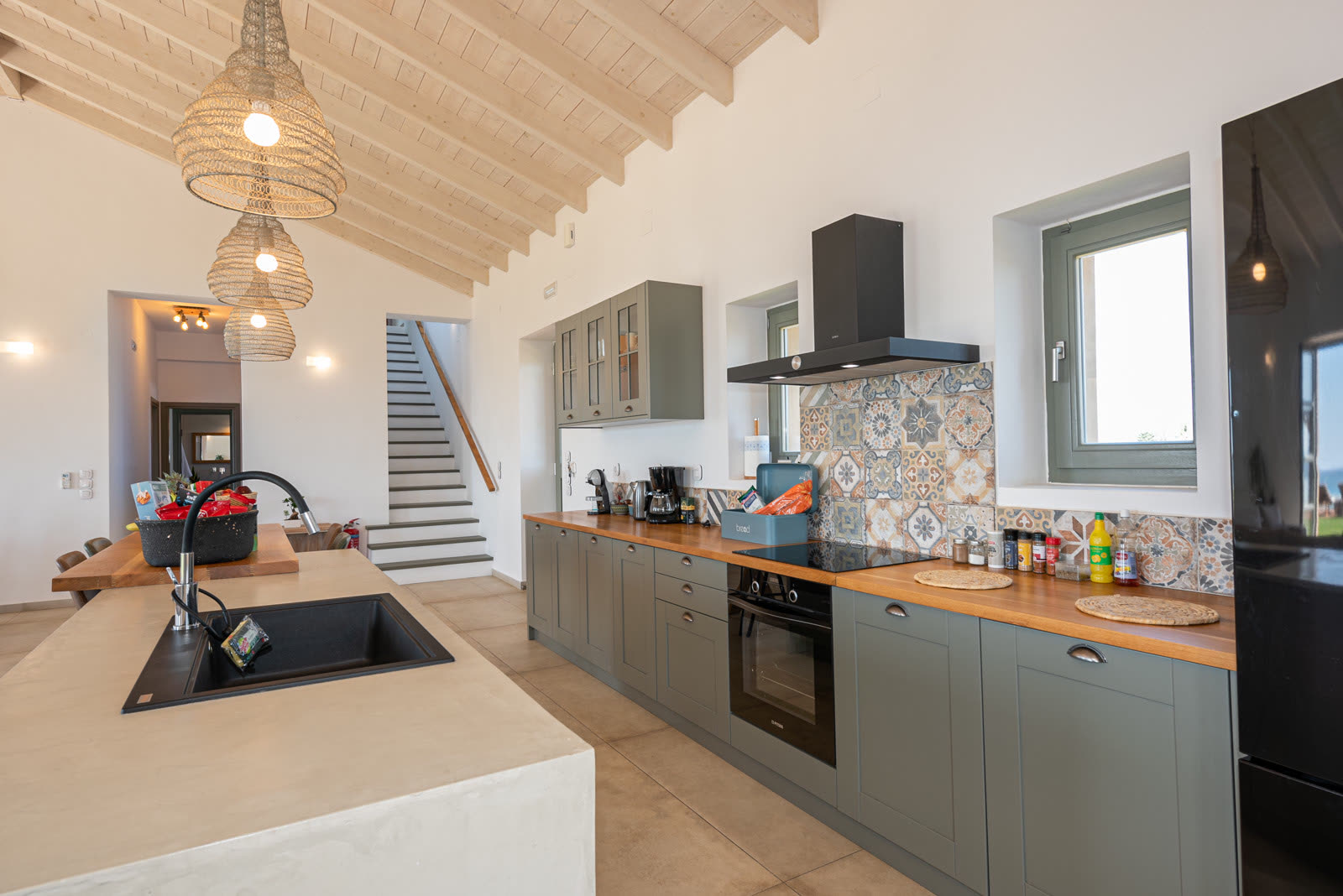 Open kitchen with sage cabinetry, island with sink and vaulted wood ceiling